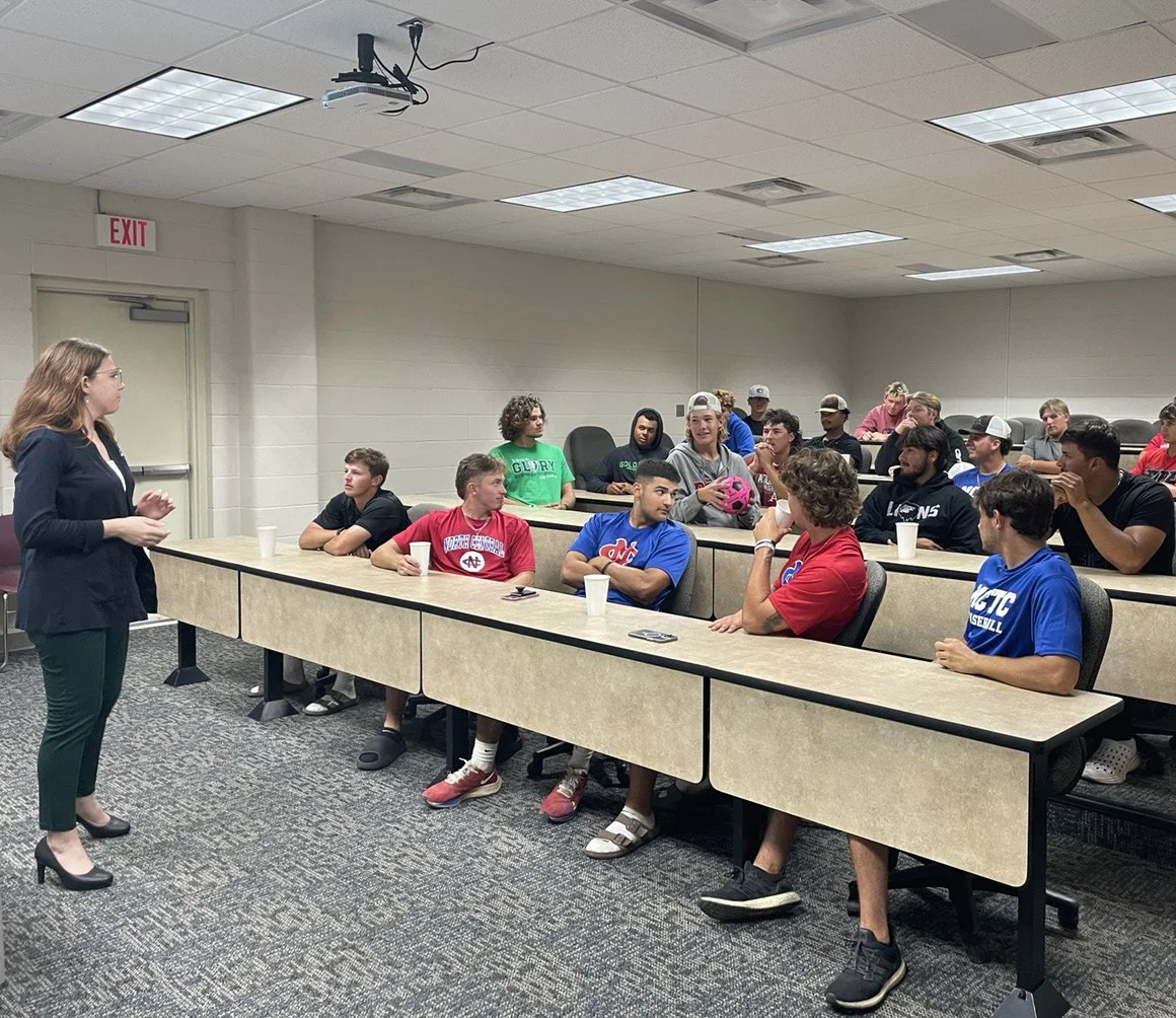A speaker engages a packed classroom as students listen, discuss, and lean in during an interactive session.